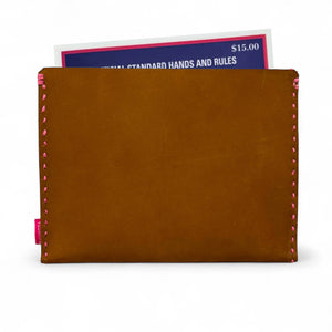 Brown leather cardholder with pink stitching holding a book on a white background